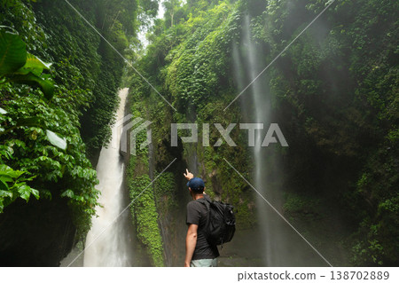 A person stands by waterfalls surrounded by green plants A person stands by waterfalls surrounded by green plants 138702889