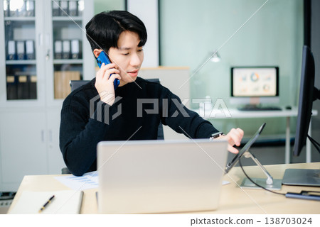 Young Asian businessman analyzing charts and talking on smartphone in office. Concept of financial reporting, remote work Young Asian businessman analyzing charts and talking on smartphone in office. Concept of financial reporting, remote work 138703024