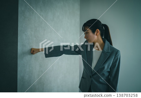 A company employee with a gloomy expression thrusts his fist against the wall. 138703258