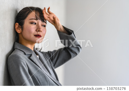 一名女子倚牆而立，一手扶著額頭。 138703276