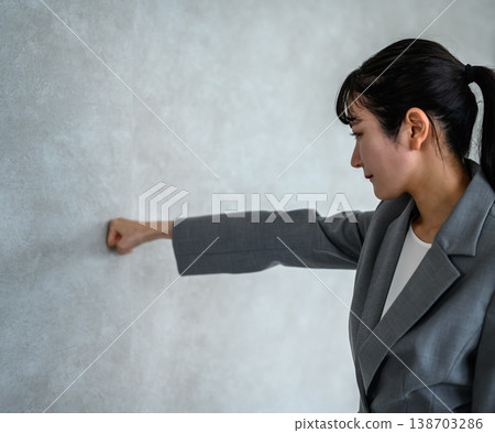 A troubled businesswoman clenches her fist against the wall. 138703286