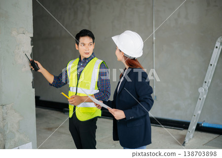 Asian engineers inspecting construction progress. Man in safety vest measures wall while female engineer Asian engineers inspecting construction progress. Man in safety vest measures wall while female engineer 138703898