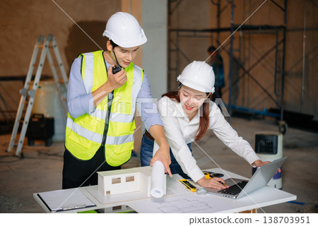 Asian engineers discuss floor plan using laptop and building model at active construction site. Collaboration, safety 138703951