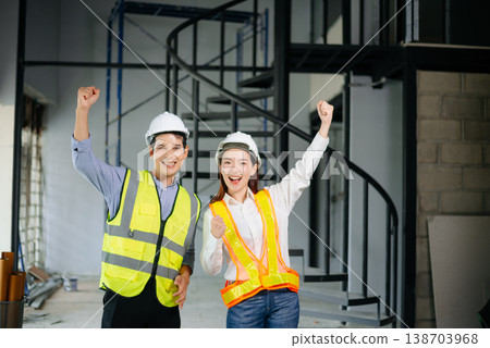 Asian engineers in safety vests and hard hats smiling on a construction site. Teamwork, pride, and professionalism in architecture 138703968
