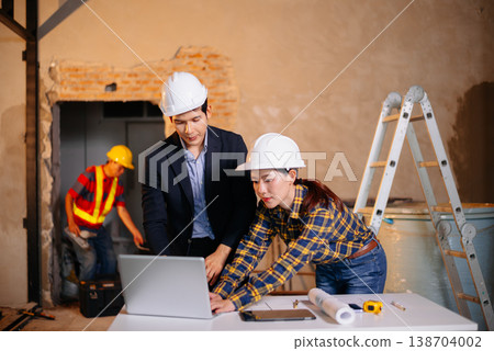 Two Asian colleagues discussing data working and tablet, laptop with architectural project at construction site 138704002