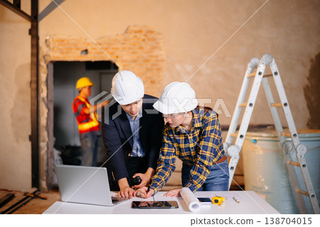 Two Asian colleagues discussing data working and tablet, laptop with architectural project at construction site 138704015