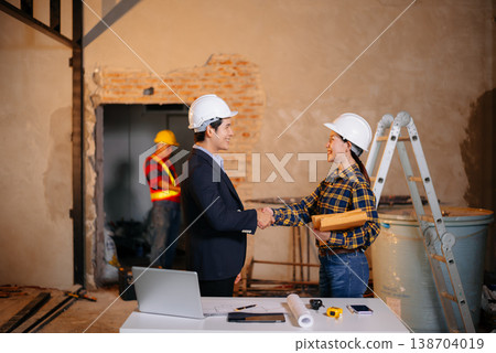Asian construction professionals shaking hands in agreement at an indoor site. Asian construction professionals shaking hands in agreement at an indoor site. 138704019