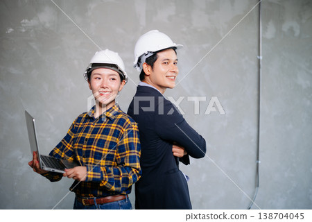 Asian construction professionals in hard hats, discussing plans with a walkie-talkie and clipboard. Indoor site teamwork Asian construction professionals in hard hats, discussing plans with a walkie-talkie and clipboard. Indoor site teamwork 138704045