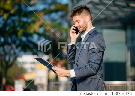 businessman works outdoors near the office holds a tablet, smiles reads good news businessman works outdoors near the office holds a tablet, smiles reads good news 138704176