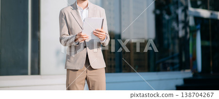 Successful Businessman in suit using tablet outdoors. Perfect for corporate, technology, and professional themes Successful Businessman in suit using tablet outdoors. Perfect for corporate, technology, and professional themes 138704267
