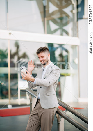 businessman works outdoors near the office holds a tablet, smiles reads good news businessman works outdoors near the office holds a tablet, smiles reads good news 138704293