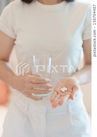 woman hand holding medicine painkiller pill and water glass on the sofa at home, taking for headaches, stomach ache, Diarrhea Pain from food poisoning, Endometriosis, Hysterectomy and Menstrual 138704487