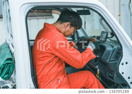 A man in overalls driving a light truck. 138705289