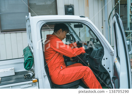 一名身穿工作服的男子駕駛著一輛輕型卡車。 一名身穿工作服的男子駕駛著一輛輕型卡車。 138705290