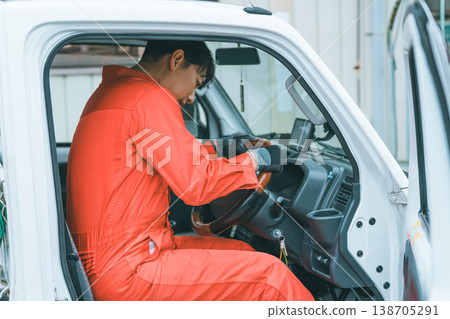 一名身穿工作服的男子駕駛著一輛輕型卡車。 138705291