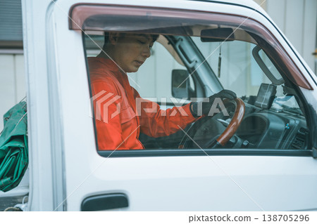 一名身穿工作服的男子駕駛著一輛輕型卡車。 一名身穿工作服的男子駕駛著一輛輕型卡車。 138705296