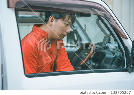 一名身穿工作服的男子駕駛著一輛輕型卡車。 一名身穿工作服的男子駕駛著一輛輕型卡車。 138705297