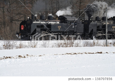 一輛蒸汽機車行駛在白雪皚皚的冬日景色中,滾滾濃煙——這是典型的北海道鐵路景象。 一輛蒸汽機車行駛在白雪皚皚的冬日景色中,滾滾濃煙——這是典型的北海道鐵路景象。 138707856