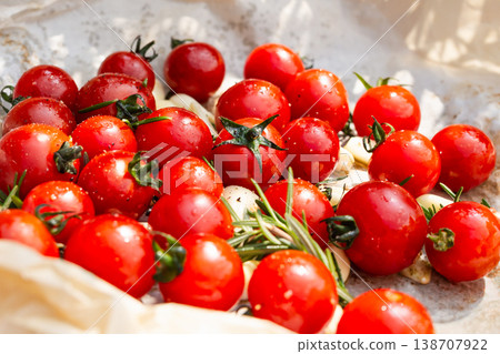 Fresh red cherry tomatoes with rosemary sprigs and garlic cloves on baking paper. Fresh red cherry tomatoes with rosemary sprigs and garlic cloves on baking paper. 138707922