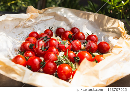 Fresh red cherry tomatoes with rosemary sprigs and garlic cloves on baking paper. Fresh red cherry tomatoes with rosemary sprigs and garlic cloves on baking paper. 138707923