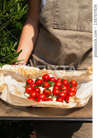 Hands holding a baking tray with fresh cherry tomatoes rosemary and garlic on parchment paper. 138707926