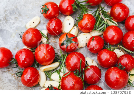 Top view of fresh cherry tomatoes garlic cloves and rosemary on baking paper. Top view of fresh cherry tomatoes garlic cloves and rosemary on baking paper. 138707928