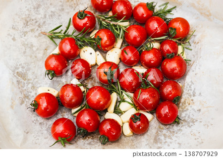 Top view of fresh cherry tomatoes garlic cloves and rosemary on baking paper. Top view of fresh cherry tomatoes garlic cloves and rosemary on baking paper. 138707929