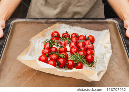 Hands holding a baking tray with fresh cherry tomatoes rosemary and garlic on parchment paper. 138707932