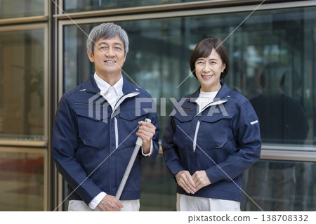 一對六十多歲的男女,穿著工作服,對著鏡頭微笑;他們看起來像是公寓大樓的管理員和物業人員。 (圖片) 一對六十多歲的男女,穿著工作服,對著鏡頭微笑;他們看起來像是公寓大樓的管理員和物業人員。 (圖片) 138708332