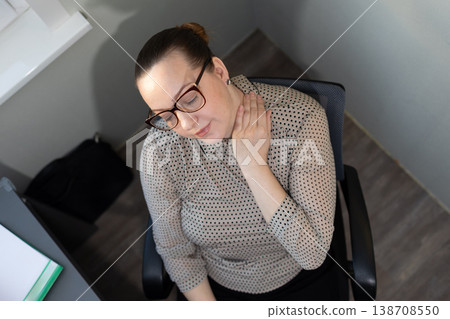 Woman in office chair rubbing her neck in discomfort. Professional experiencing workplace stress and pain. Health and ergonomics concept for desk job awareness. Woman in office chair rubbing her neck in discomfort. Professional experiencing workplace stress and pain. Health and ergonomics concept for desk job awareness. 138708550