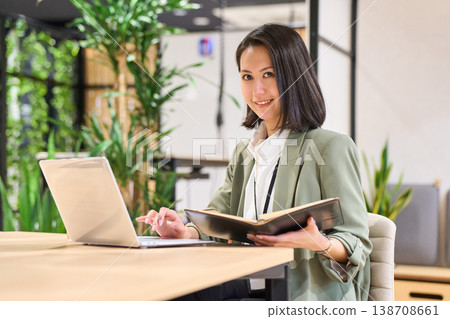A female systems engineer taking notes while looking at her smartphone in the office of a foreign-owned IT company. A female systems engineer taking notes while looking at her smartphone in the office of a foreign-owned IT company. 138708661