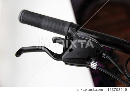 A detailed close-up of a black bicycle handlebar with a brake lever and textured grip on a light background, highlighting the modern design, handling and urban cycling style. 138708946