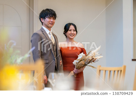 The bride and groom enter the reception hall with a bouquet at their wedding (after changing outfits). The bride and groom enter the reception hall with a bouquet at their wedding (after changing outfits). 138709429