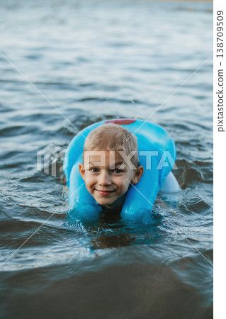 Smiling child swims in the water in a protective inflatable vest. Child safety. The safety of children in the pond. Smiling child swims in the water in a protective inflatable vest. Child safety. The safety of children in the pond. 138709509