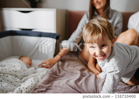 Smiling Toddler Playing Near Newborn In Bed Smiling Toddler Playing Near Newborn In Bed 138710400
