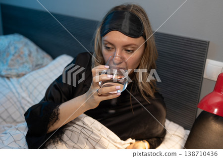 Woman in silk nightgown drinking water from glass in dim bedroom photography Woman in silk nightgown drinking water from glass in dim bedroom photography 138710436