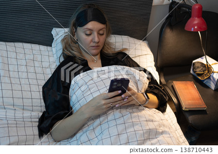 Woman in black silk robe checking smartphone in dim bedroom at night. photography 138710443