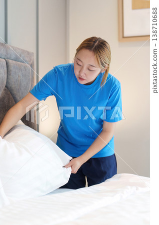 Housekeeper arranging bed linens and organized bedroom Housekeeper arranging bed linens and organized bedroom 138710688