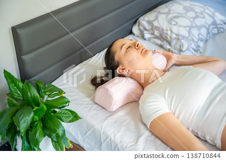 Woman lying on bed using ergonomic orthopedic pillow for cervical spine support. Proper neck alignment during sleep for posture correction, muscle relaxation, pain relief and comfortable healthy rest Woman lying on bed using ergonomic orthopedic pillow for cervical spine support. Proper neck alignment during sleep for posture correction, muscle relaxation, pain relief and comfortable healthy rest 138710844