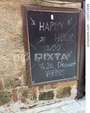 Chalkboard sign displaying happy hour times and beer discount outside on rustic stone wall Chalkboard sign displaying happy hour times and beer discount outside on rustic stone wall 138713606