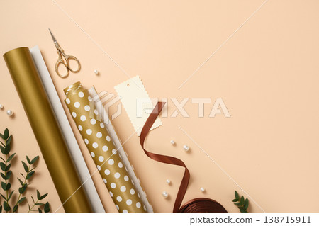 Gift wrapping background. Paper rolls, gift tag, and pearls on beige desk. Copy space for holiday text or design. Gift wrapping background. Paper rolls, gift tag, and pearls on beige desk. Copy space for holiday text or design. 138715911