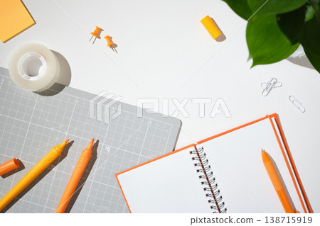 Orange stationery and crafting tools on a white background. Open blank notebook, markers, cutting mat, tape, and push pins with copy space. Orange stationery and crafting tools on a white background. Open blank notebook, markers, cutting mat, tape, and push pins with copy space. 138715919