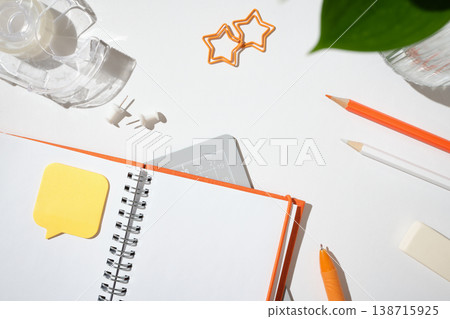 Open notebook with a speech bubble sticky note, orange pen, and star-shaped paper clips on a white desk. Copyspace Open notebook with a speech bubble sticky note, orange pen, and star-shaped paper clips on a white desk. Copyspace 138715925