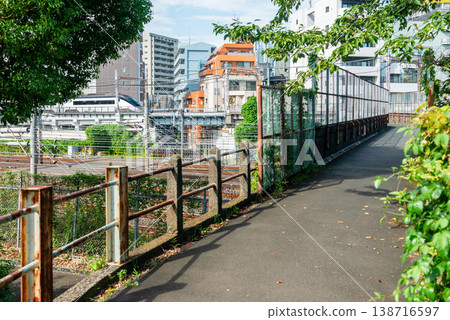 從鶯谷站到日暮里站之間的天橋上可以看到京成線列車,鏽跡斑斑的圍欄和綠樹環繞的人行道。 從鶯谷站到日暮里站之間的天橋上可以看到京成線列車,鏽跡斑斑的圍欄和綠樹環繞的人行道。 138716597
