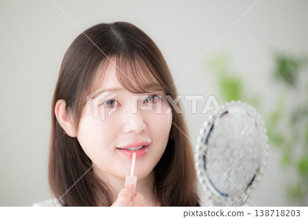 一位女士對著手鏡塗抹口紅,展示了她的自然妝容和美容護理程序,包括唇彩和唇部護理。 一位女士對著手鏡塗抹口紅,展示了她的自然妝容和美容護理程序,包括唇彩和唇部護理。 138718203