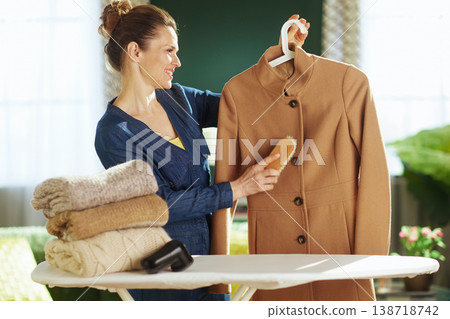 Smiling Woman Maintaining Outerwear with a Clothes Brush Smiling Woman Maintaining Outerwear with a Clothes Brush 138718742