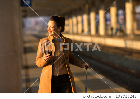 Smiling Woman with Suitcase Waiting for Train in Sunlight Smiling Woman with Suitcase Waiting for Train in Sunlight 138719245