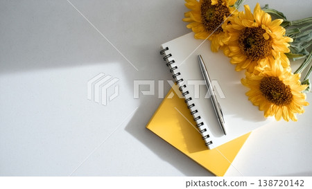 白色背景上的桌上放著一本打開的筆記本和一支筆；向日葵。 138720142