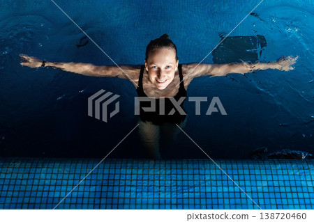 Above top view portrait of young adult caucasian female model in sport black swimsuit stand in clear blue water of indoor swimming pool at dark evening time. Relax harmony and wellness spa therapy 138720460