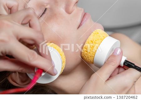 Close-up beautician doctor hand making anti-age face remodel procedure treatment with hardware microcurrent electric tool attractive young 30-40 female model at beauty clinic. Cosmetologist skincare Close-up beautician doctor hand making anti-age face remodel procedure treatment with hardware microcurrent electric tool attractive young 30-40 female model at beauty clinic. Cosmetologist skincare 138720462